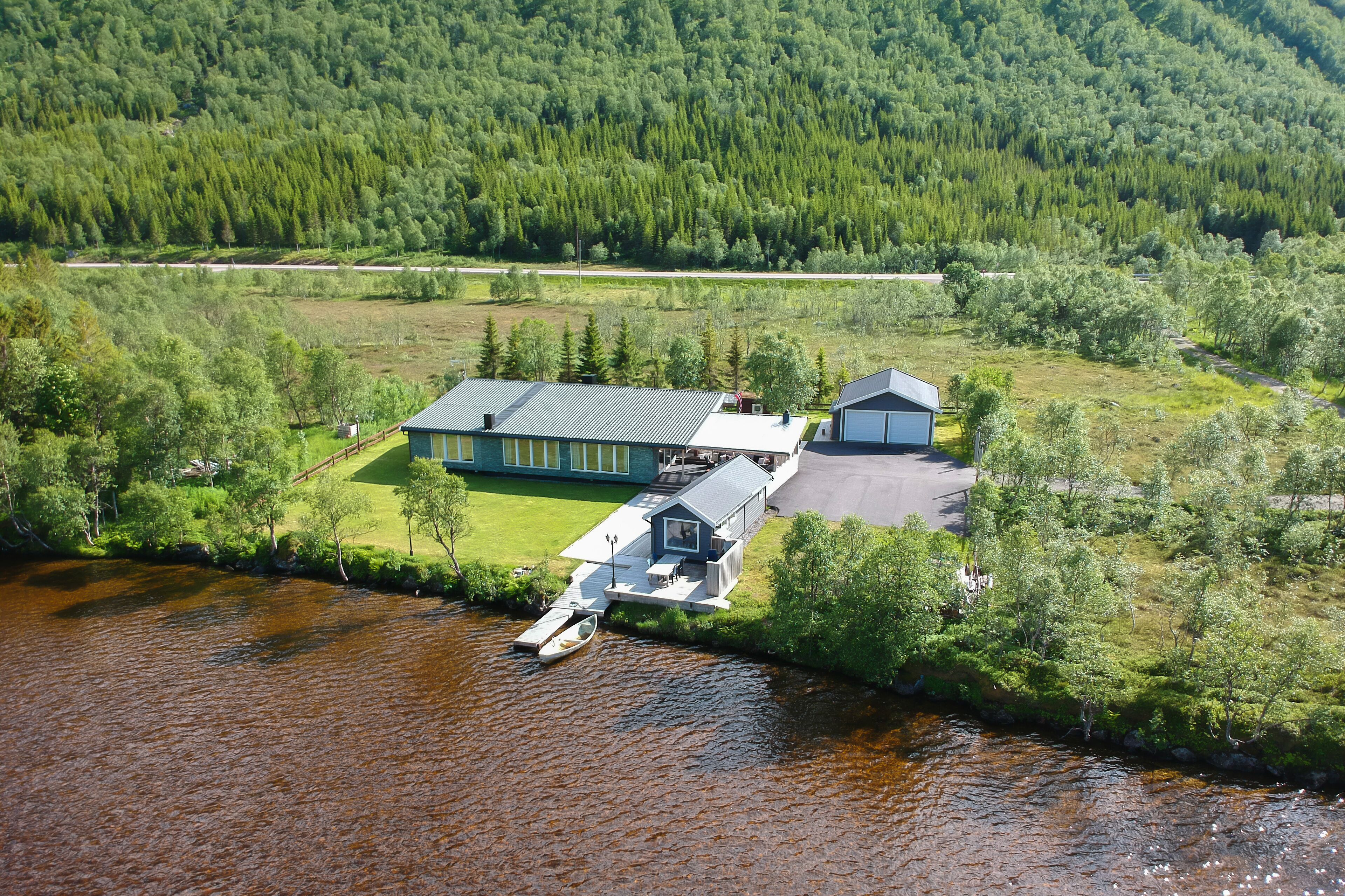 Une propriété au bord du lac comprenant une maison principale, un bâtiment plus petit et un quai avec un bateau.