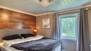 A bedroom with a wooden headboard, a large window with curtains, and a chandelier. - VESTERALEN LODGE - TOP QUALITY IN THE VESTERALEN and LOFOTEN (Sortland)