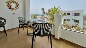 Ein Balkon mit Tisch und Stühlen, einem dekorativen Kranz und Blick auf Palmen und Gebäude.