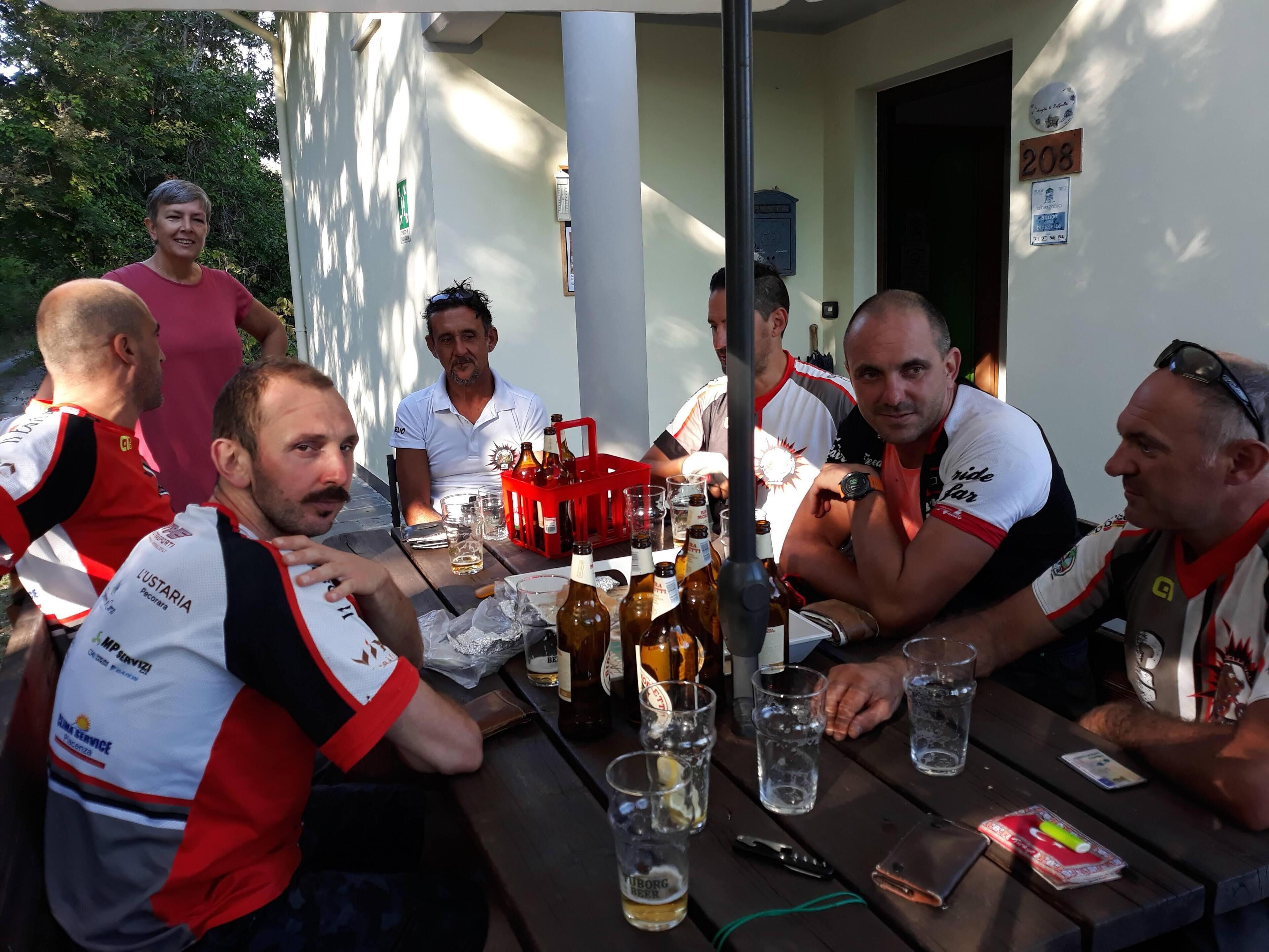 A group of people seated at an outdoor table with various bottles and glasses, suggesting a social gathering.
