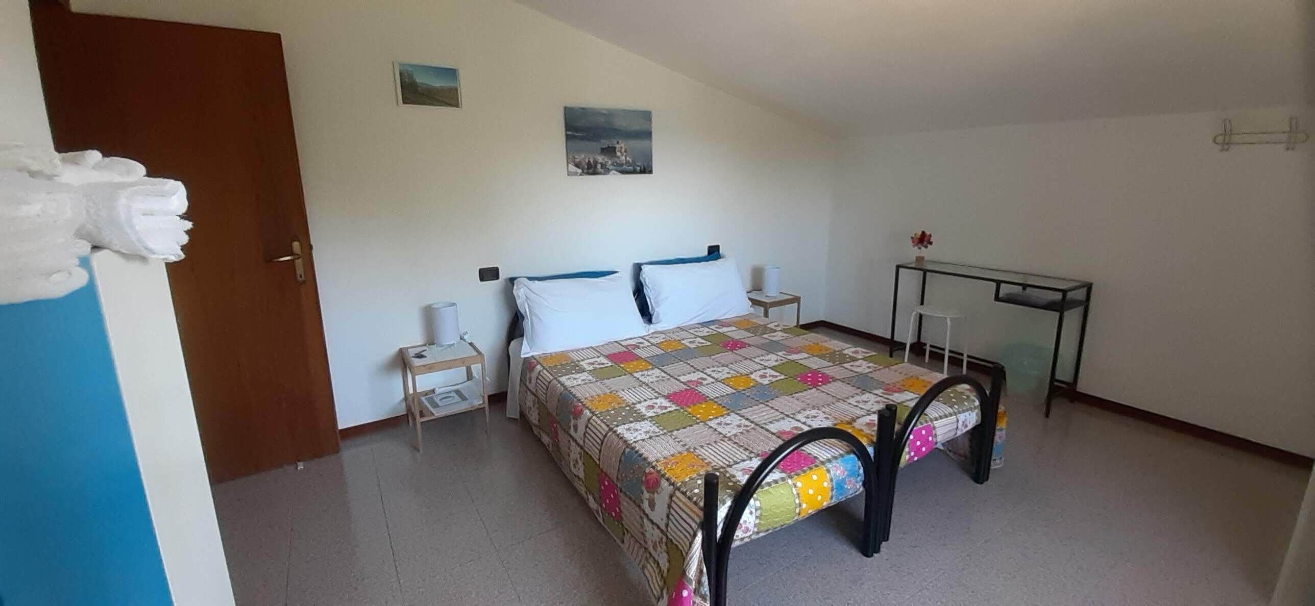 A bedroom with a bed, bedside tables, a small table, and a wall-mounted shelf.