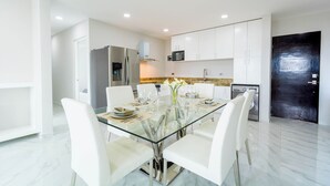 Una cocina moderna con armarios blancos, una mesa de comedor de vidrio y sillas blancas.