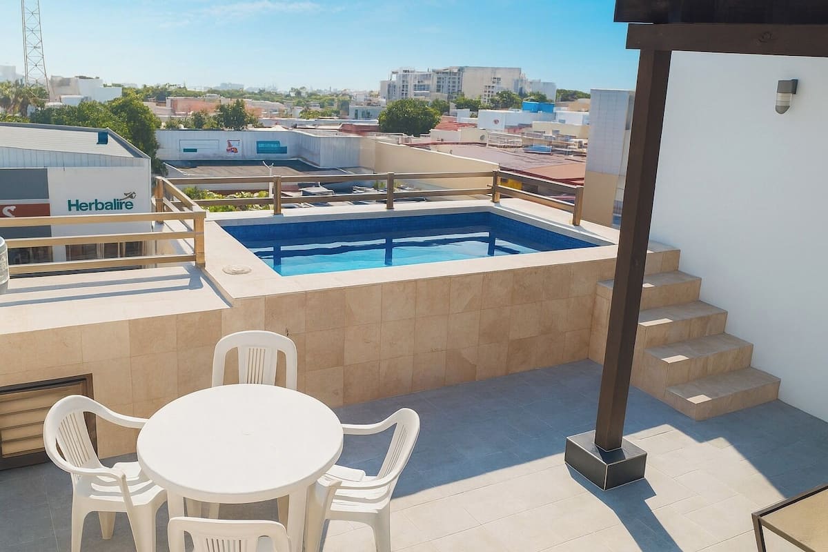 Una terraza en la azotea con piscina, mesa y sillas, y una escalera.