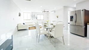 Una cocina moderna con un refrigerador de acero inoxidable, una mesa de comedor con sillas y un sofá blanco al fondo.