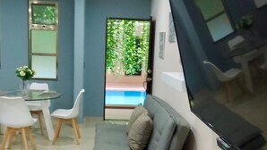 Una sala moderna con un sofá gris, una mesa de comedor con sillas, un televisor de pantalla plana montado en la pared y vista a una piscina a través de una puerta de vidrio.