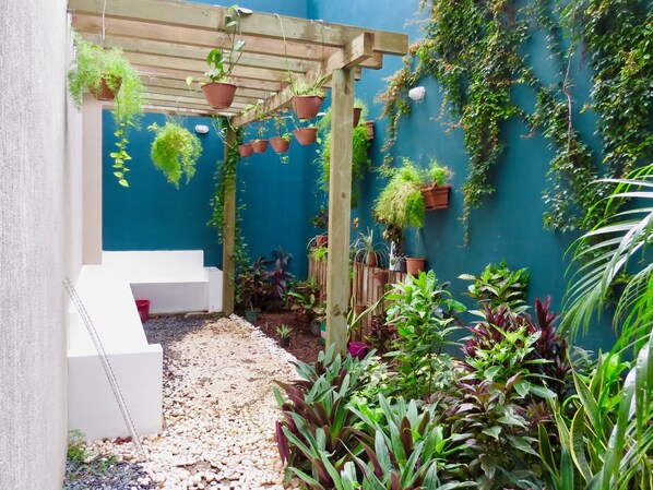 A covered garden area with a wooden pergola, potted plants, and a white bench.
