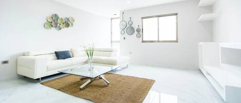 A modern living room with a white sofa, a glass coffee table, and a ceiling fan.