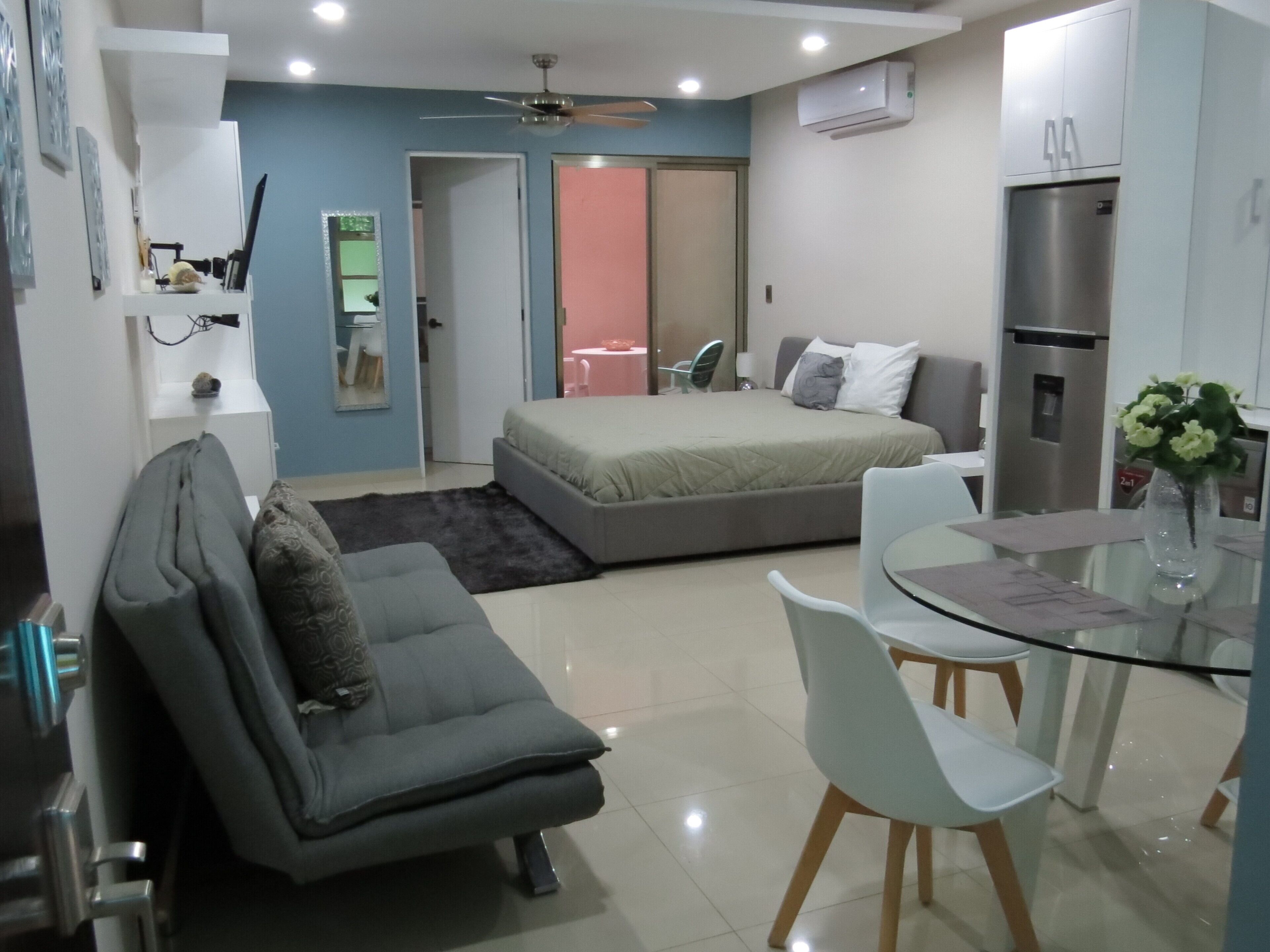 Een compacte hotelkamer met een bed, een bank, een eettafel en een kitchenette.