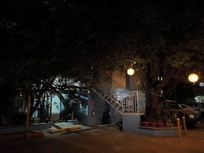 A nighttime outdoor area with a staircase leading to a building, surrounded by trees and potted plants.