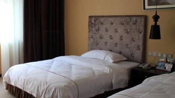 A hotel room with a large bed, a bedside table with a lamp, and a framed picture on the wall. - Kai Te Hotel (Chongqing)
