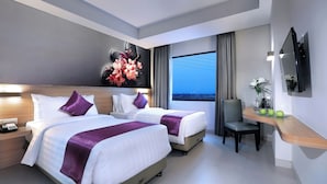 A hotel room with two beds, a desk, a chair, a television, and a large window with a city view. - Quest Prime Cikarang by Aston (Cikarang)