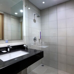 A modern bathroom with a black countertop, a white sink, a large mirror, and a shower area.