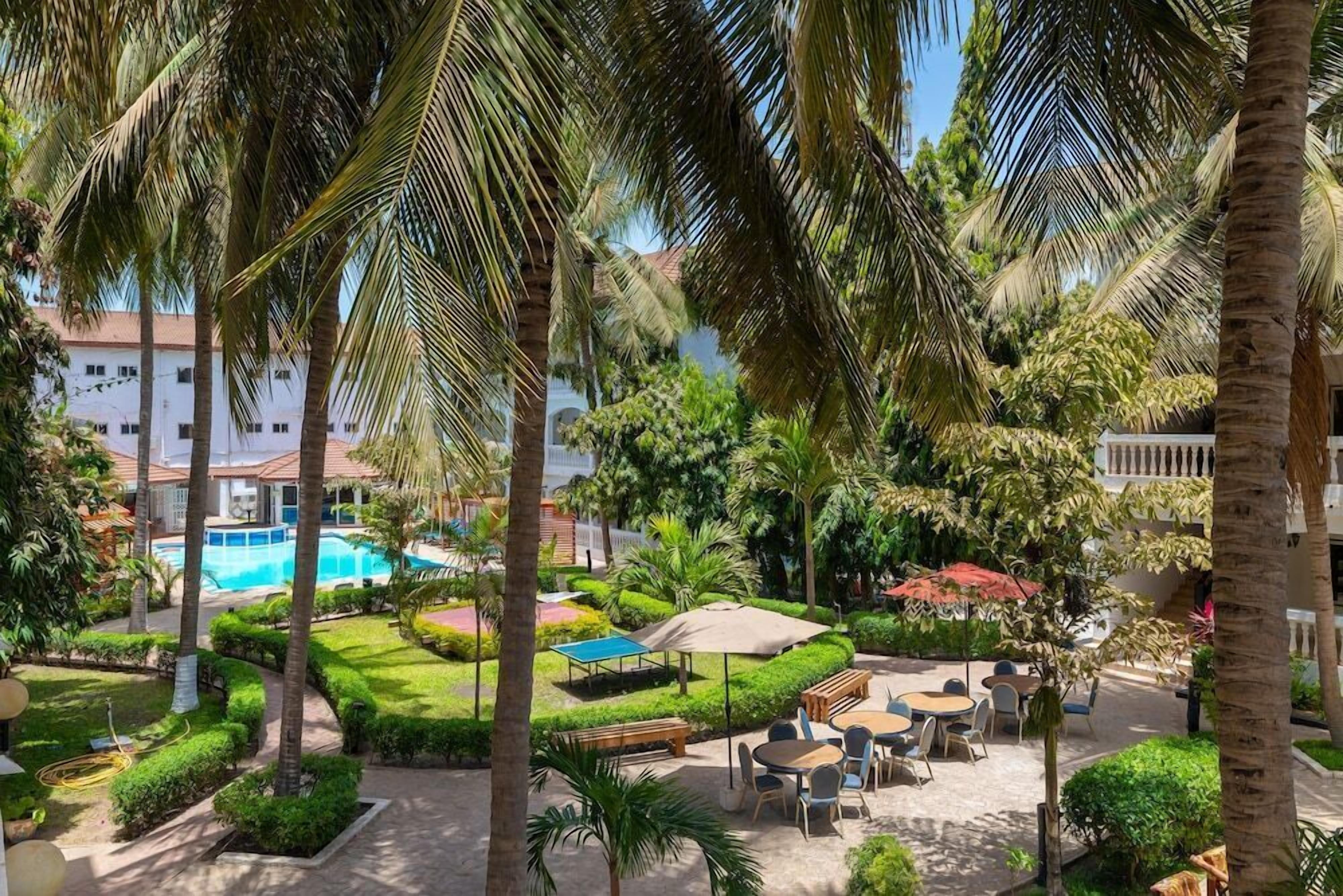 A resort courtyard with a swimming pool, palm trees, and outdoor seating areas.