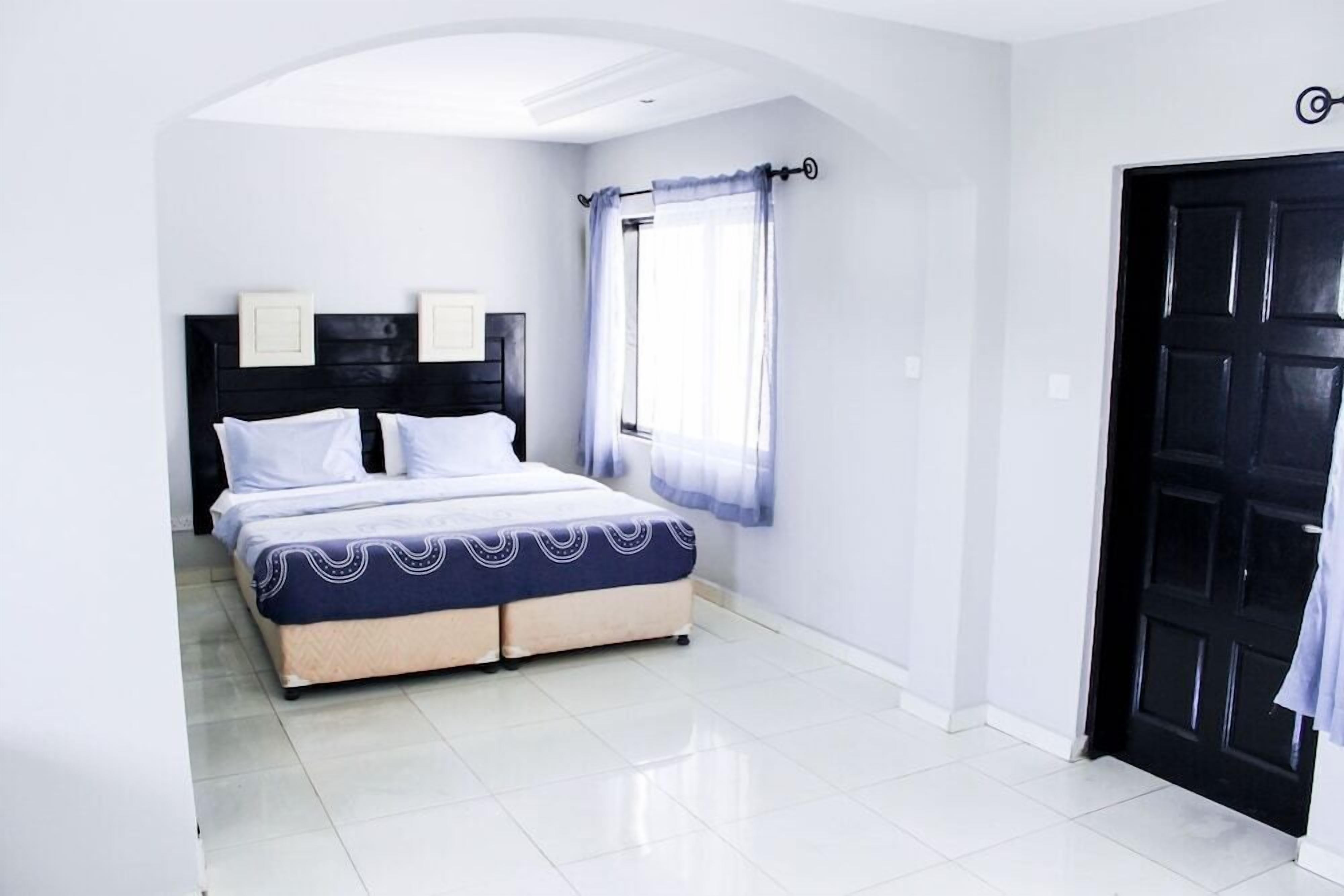 A bedroom with a bed, a window with curtains, a black door, and a white wall.