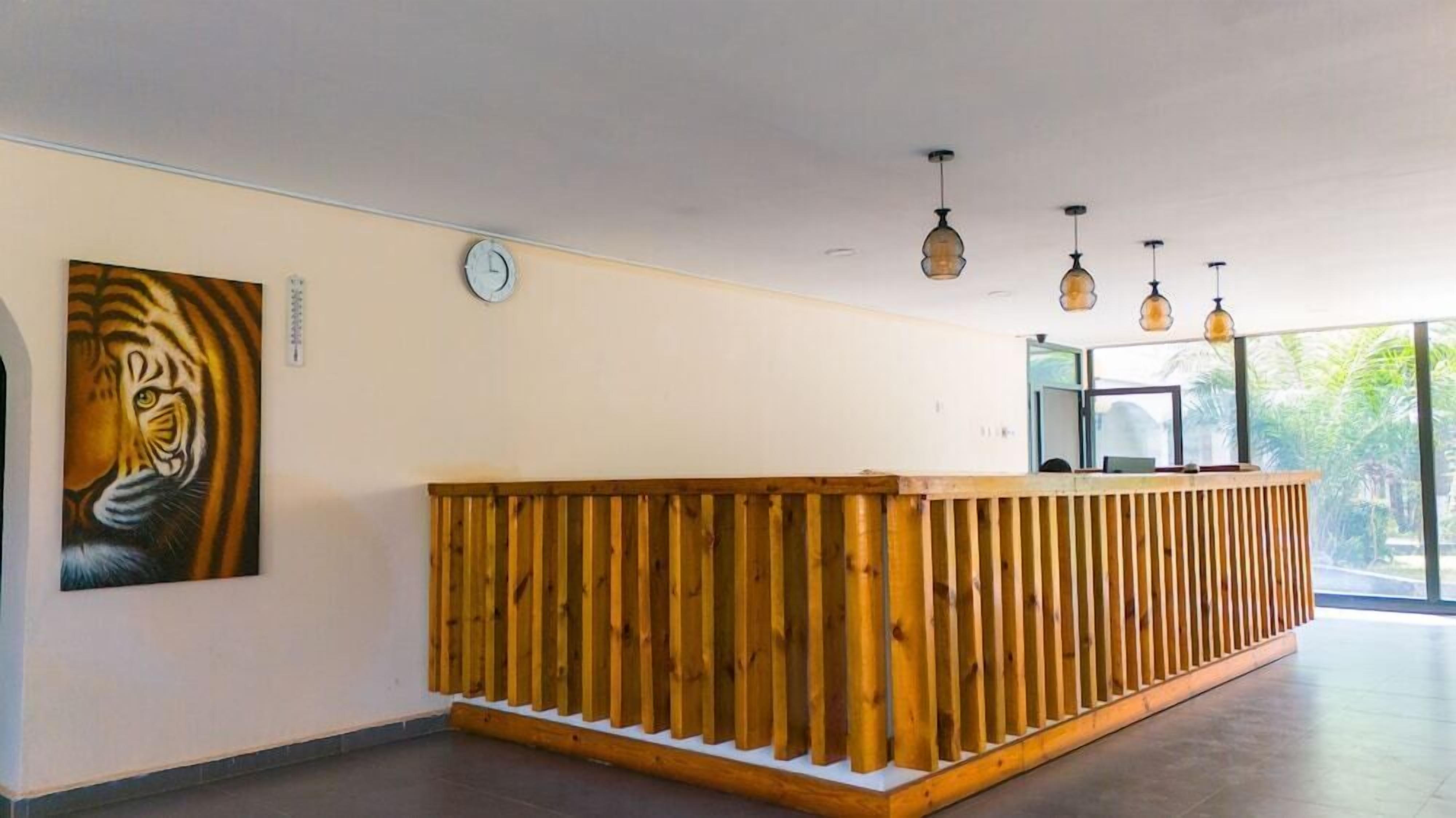 A reception desk with a wooden slat design, a clock on the wall, and pendant lighting.