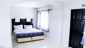 Un dormitorio con cama, ventana con cortinas, puerta y cabecera con decoración de pared.