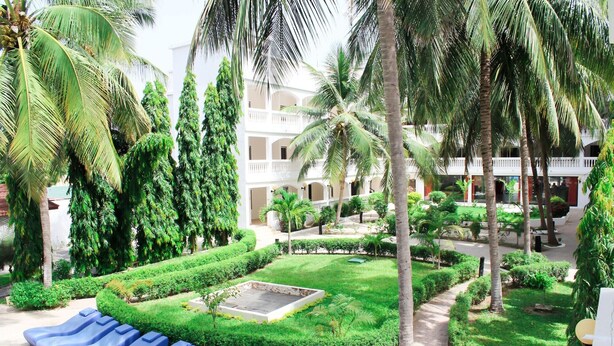 Un patio con palmeras, una piscina con tumbonas azules y un edificio con balcones.