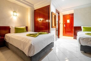 Habitación de hotel con dos camas, una puerta de madera, un espejo y una lámpara de pared.