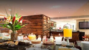 A buffet area with various food items, a juice dispenser, and a decorative plant. - Golden Tulip Macae (Macaé)