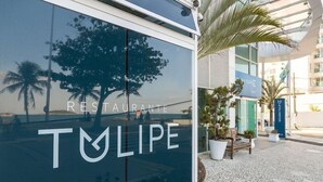 A restaurant named 'TULIPE' with a modern glass facade reflecting palm trees and a building in the background. - Golden Tulip Macae (Macaé)