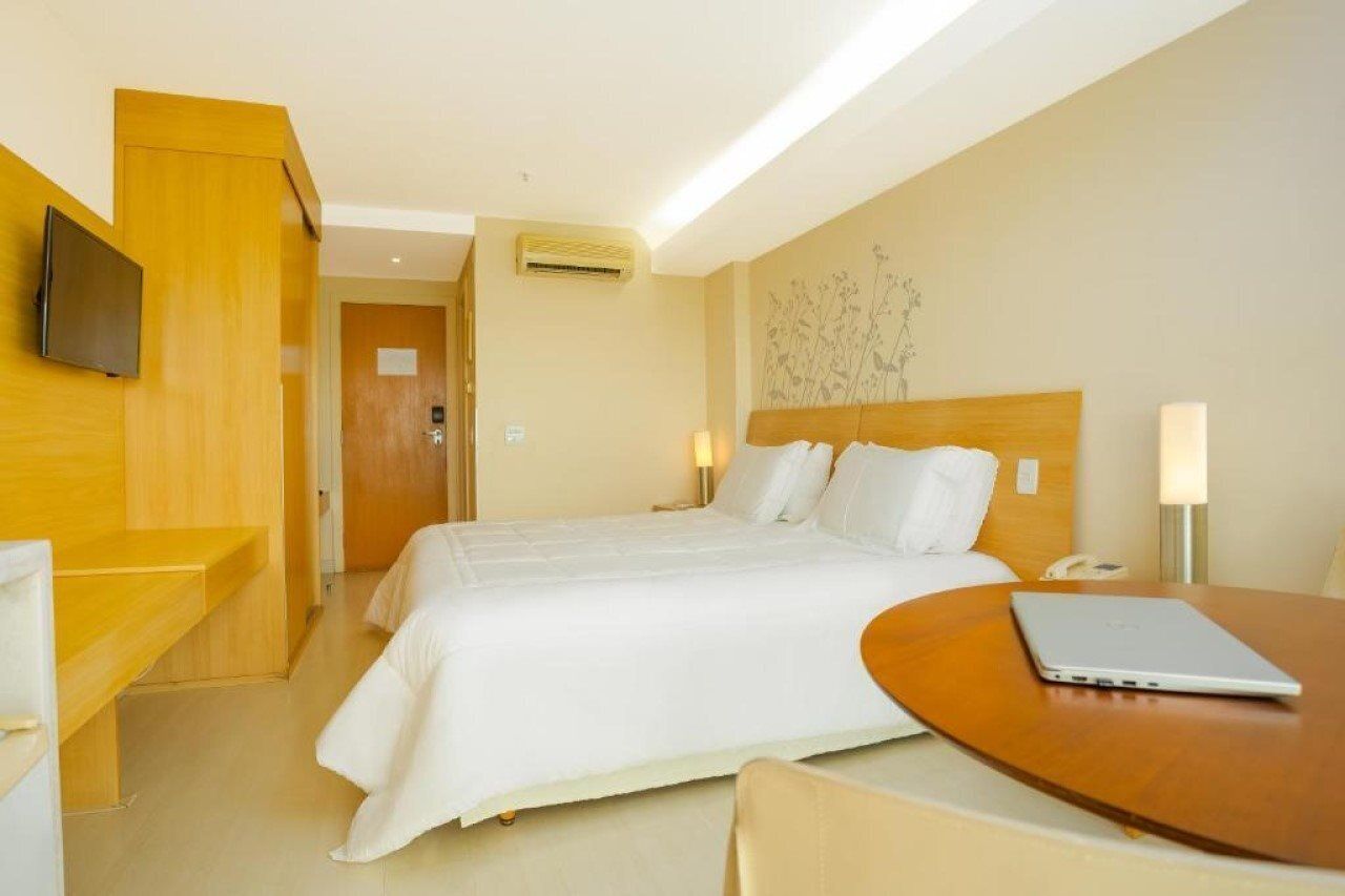 A hotel room with a bed, a desk, a laptop, and a TV.