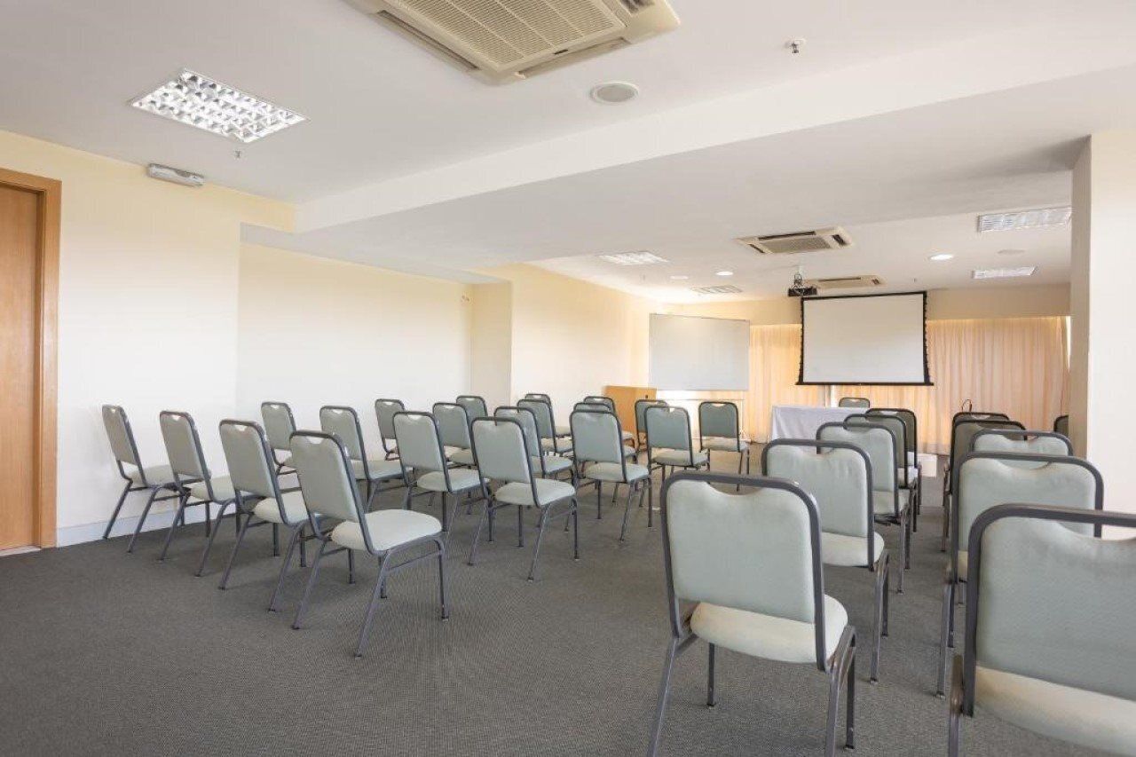 Un salón de conferencias con filas de sillas, una pantalla de proyector y una pizarra.