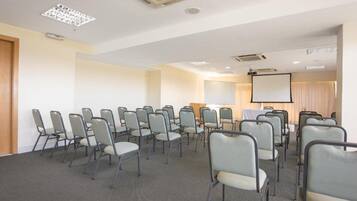 Un salón de conferencias con filas de sillas, una pantalla de proyector y una pizarra.