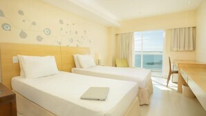 A hotel room with two beds, a desk, and a view of the sea. - Golden Tulip Macae (Macaé)