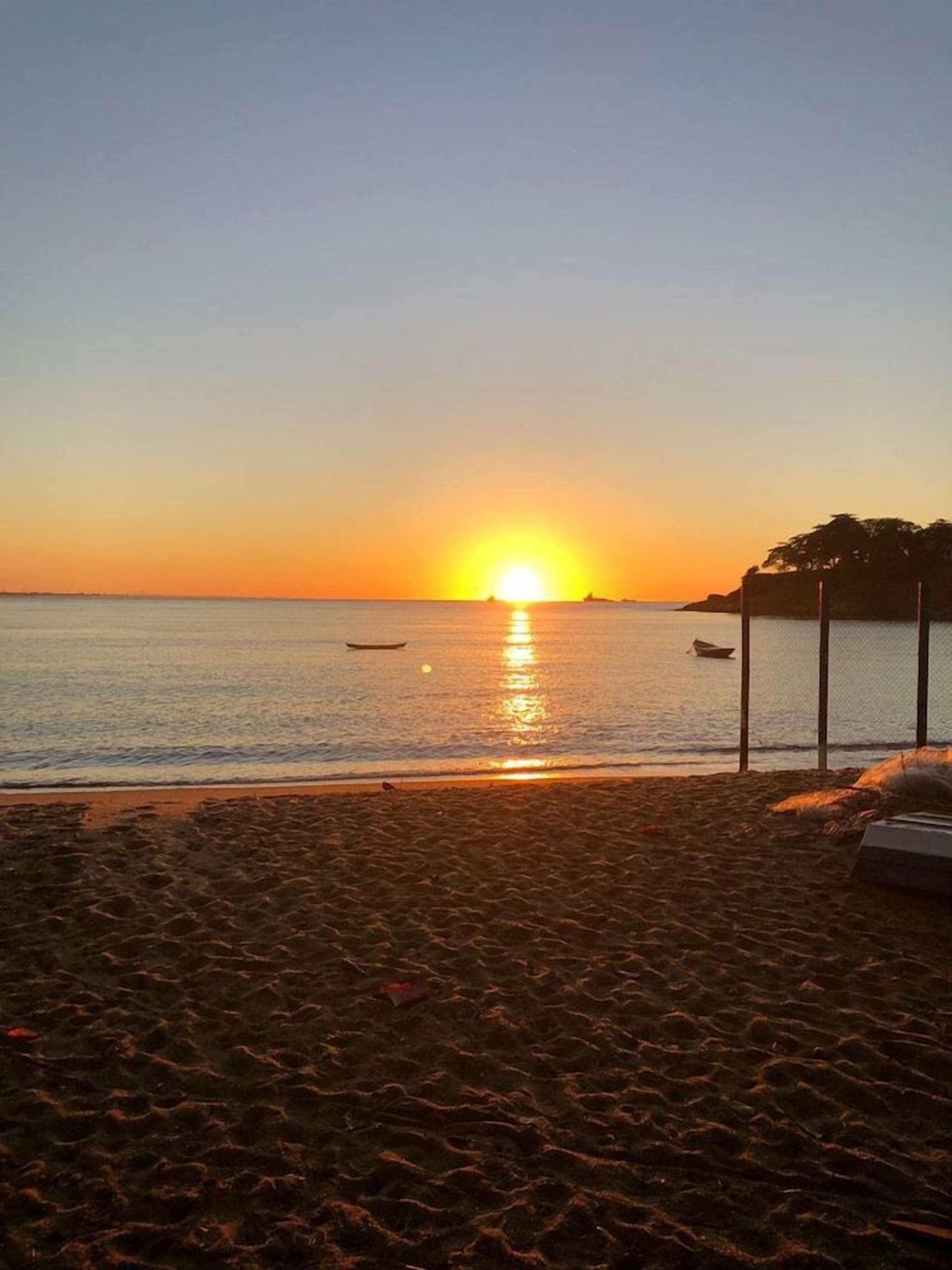 Una playa al atardecer con aguas tranquilas, un bote y una cerca.
