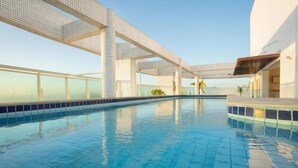 A swimming pool with tiled flooring and a clear blue sky in the background. - Golden Tulip Macae (Macaé)
