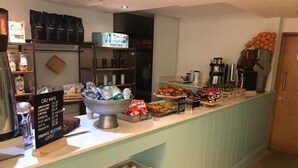 Mostrador de una cafetería con una pizarra de menú, un bol de pasteles y una máquina de café.