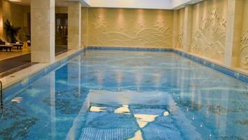 A large indoor swimming pool with a glass ceiling, surrounded by walls with wave patterns.