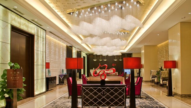 Un hall de hotel con un mostrador de recepción, sillas rojas, una lámpara roja, un candelabro y una escultura roja.