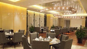 Un comedor amplio de hotel con varias mesas y sillas, un candelabro grande y cortinas decorativas.