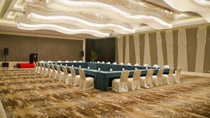 Un salón de conferencias con una larga mesa, sillas blancas y una alfombra estampada.