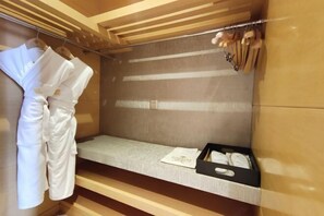 A small, private room with a bed, a bedside table, and a robe hanging on a rack.