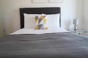 A neatly made bed with a black headboard, a white pillow, and a geometric-patterned pillow. - Quay Apartments Newport (Newport)