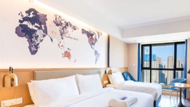 A hotel room with two beds, a world map on the wall, and a city view through the window. - Kyriad Marvelous Hotel (Xi'an)