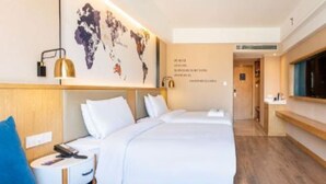 A hotel room with a large bed, a desk with a lamp, a world map on the wall, and a TV mounted on the wall.