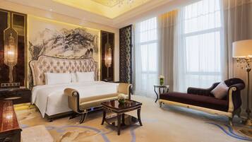 A luxurious bedroom with a large bed, a chaise lounge, a small table, and a chandelier.