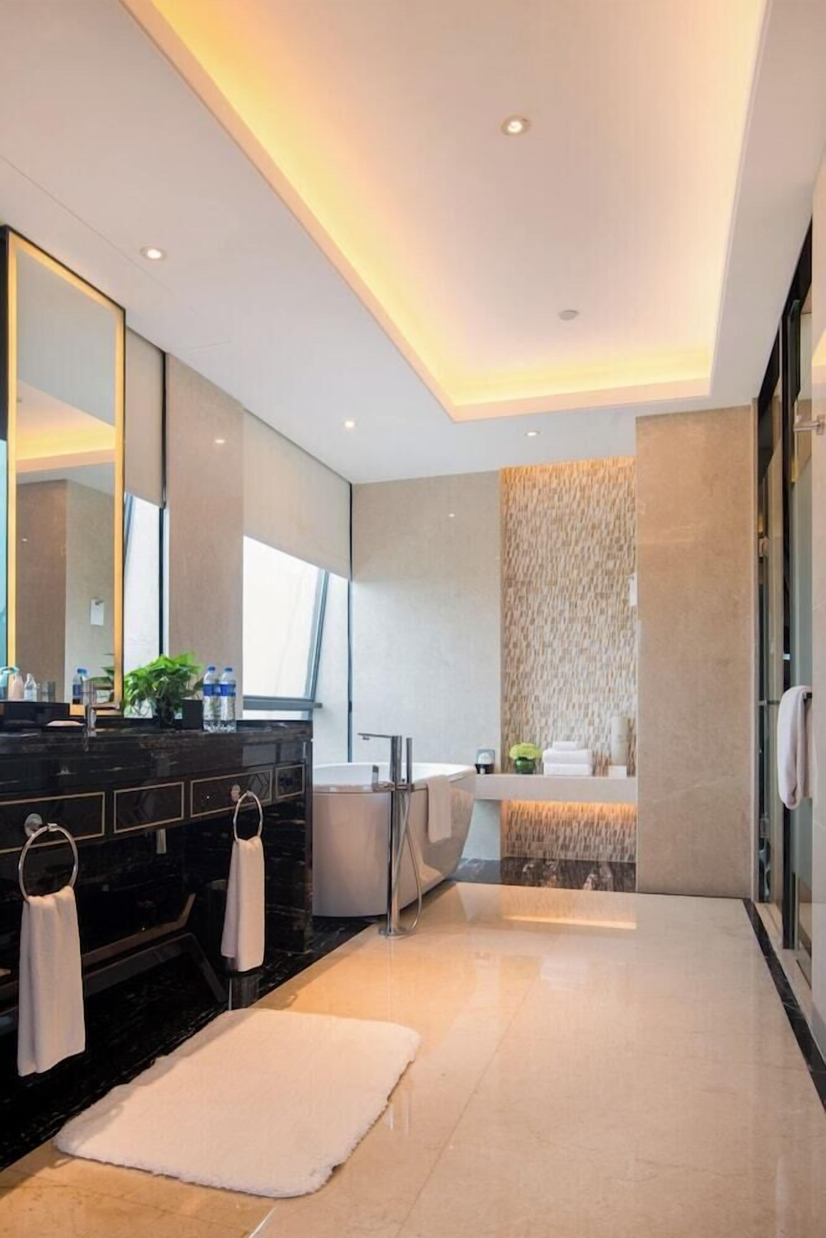 A modern bathroom with a large mirror, a bathtub, and a vanity with a dark countertop.