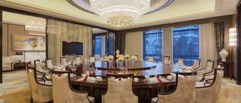 A spacious conference room with a large round table, multiple chairs, and a chandelier.