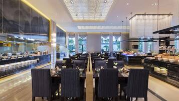 A modern dining area with multiple tables and chairs, a central walkway, and a kitchen area with food displays.
