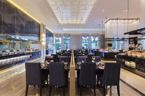 A modern dining area with multiple tables and chairs, a central walkway, and a kitchen area with food displays. - Wanda Realm Guangzhou Zengcheng (Guangzhou)