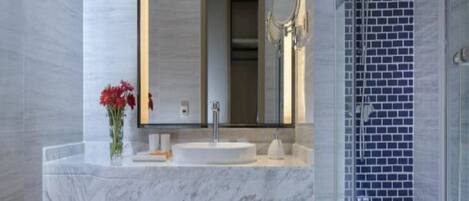 A modern bathroom with a marble sink, a large mirror, and a shower with blue mosaic tiles.