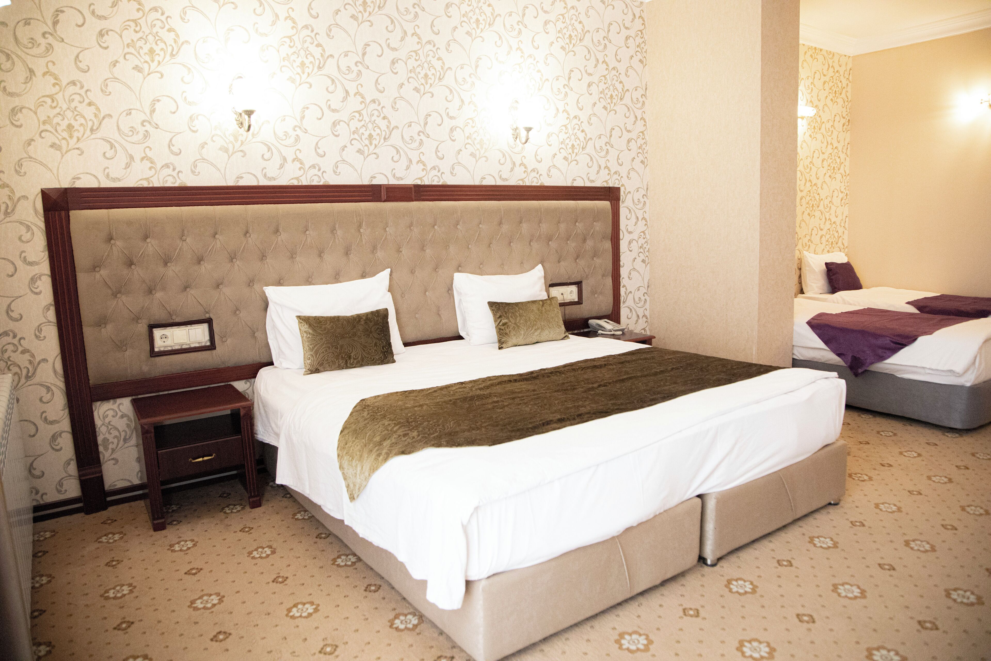 A hotel room with a large bed, a nightstand, a lamp, and a mirror.
