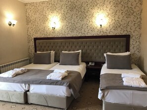 Habitación de hotel con dos camas, cada una con cabecero, almohadas y toallas. Se observan apliques de pared y un teléfono sobre la mesita de noche.