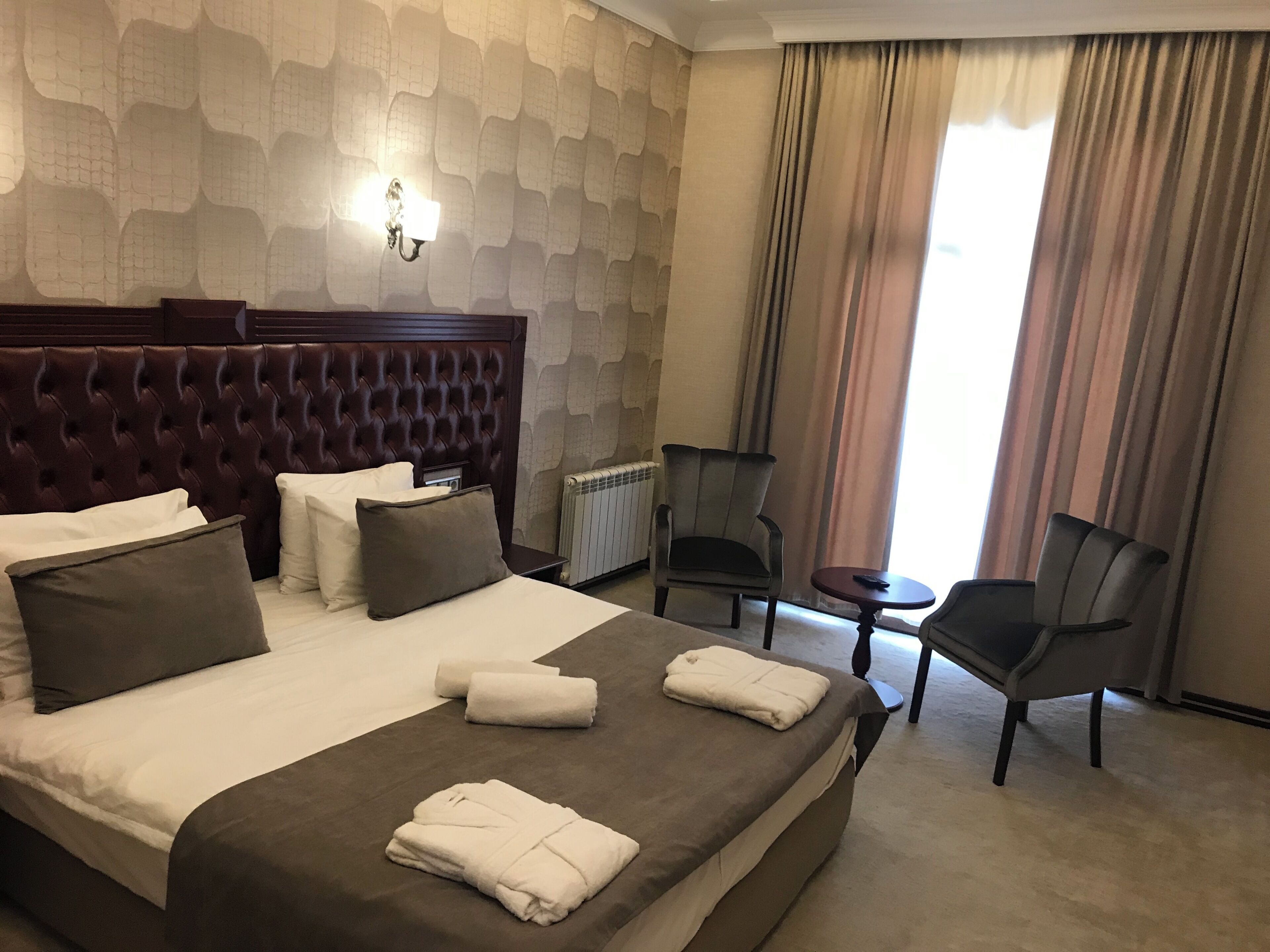 A hotel room with a large bed, a chair, a small table, and a radiator.