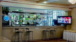 A bar area with a television screen, multiple bar stools, and a variety of bottles and glasses on shelves. - Astana International (Almaty)