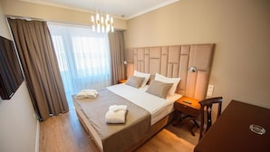 A hotel room with a large bed, a wooden desk, and a chair. - Astana International (Almaty)